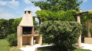 Een bakoven van baksteen buiten, met schoorsteen, omringd door groen en een pergola.