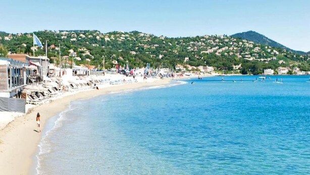 Una platja amb aigua blava cristal·lina, un tram de sorra i edificis al fons.