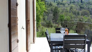 Un balcon avec une table et des chaises, une bouteille de vin et une vue sur une colline boisée.