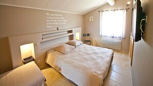Une chambre avec un grand lit, des tables de chevet, une étagère fixée au mur, un radiateur et une fenêtre avec des rideaux.