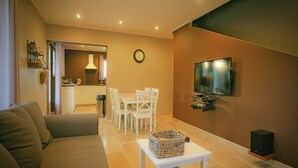 Un salon comprenant un canapé, une table à manger avec des chaises, un téléviseur fixé au mur et une petite table avec un panier.