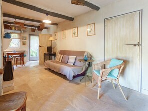 A cozy room with a bed, a wicker chair, a desk with a computer, and framed botanical prints on the wall.