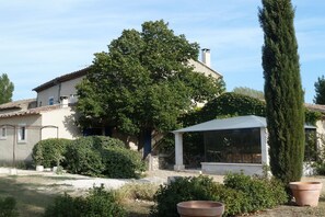 A house with a large tree, a covered patio, and a garden with potted plants.
