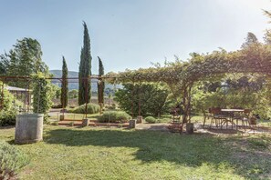A garden with a pergola, a table with chairs, and a variety of plants.