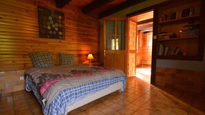 Ein gemütliches Schlafzimmer mit Holzbalkendecke, einem Bett mit karierter Decke, einem Nachttisch mit Lampe und einem Bücherregal.