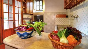 Une cuisine avec des meubles de rangement en bois, une fenêtre et un plan de travail sur lequel se trouve un saladier rempli de légumes.