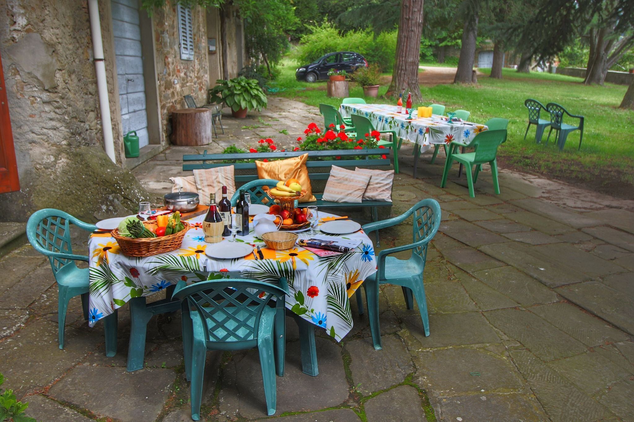 An outdoor dining area with stone flooring, green plastic chairs, and tables set with plates, bowls, and bottles.