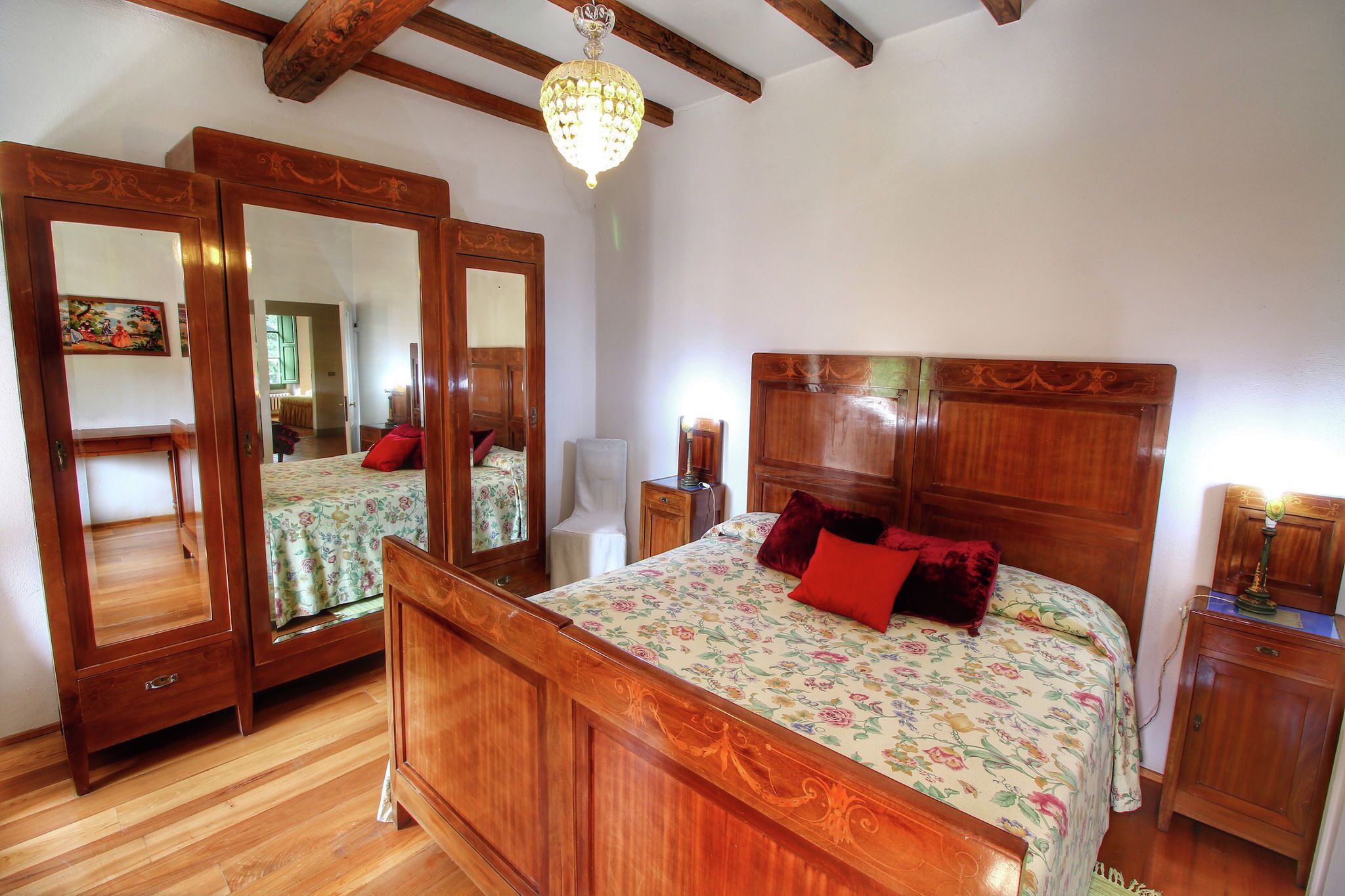 Une chambre à coucher avec un lit en bois, un grand miroir, un lustre et une table de chevet.