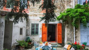 Une cour rustique avec un mur de pierre, des volets en bois et des plantes en pot.