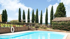 A swimming pool with a clear blue water, surrounded by a brick wall, and a metal railing.