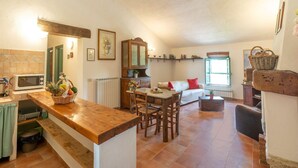 A cozy kitchen with a wooden counter, a dining area with chairs, a sofa, and a window with a view.