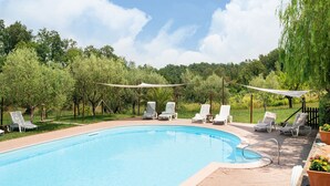A swimming pool with lounge chairs and a shaded area, surrounded by trees and greenery. - Belvilla by OYO Il Bosco (Collesalvetti (LI))