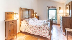 A bedroom with a wooden bed, a nightstand, a dresser, and a window with a view.