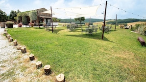 An outdoor seating area with tables and chairs, a building with a tiled roof, and a grassy field with trees in the background. - Apartment near Pisa, Beaches (Collesalvetti (LI))