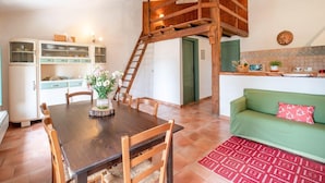A dining area with a wooden table and chairs, a kitchen with a green wall and tiled backsplash, and a loft bedroom with a wooden staircase. - Apartment near Pisa, Beaches (Collesalvetti (LI))