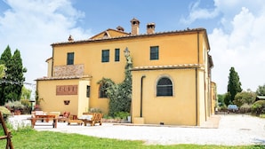 A two-story building with a yellow facade, a small garden with outdoor seating, and a clear blue sky. - Apartment near Pisa, Beaches (Collesalvetti (LI))