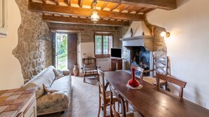 A rustic interior with exposed wooden beams, a stone wall, a fireplace, a dining table, and a sofa. - Farmhouse with pool in Michelangelo (Caprese Michelangelo)
