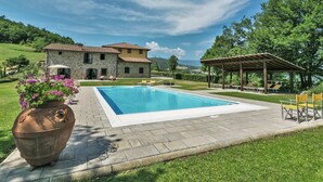 A stone house with a swimming pool, outdoor seating, and a pergola.