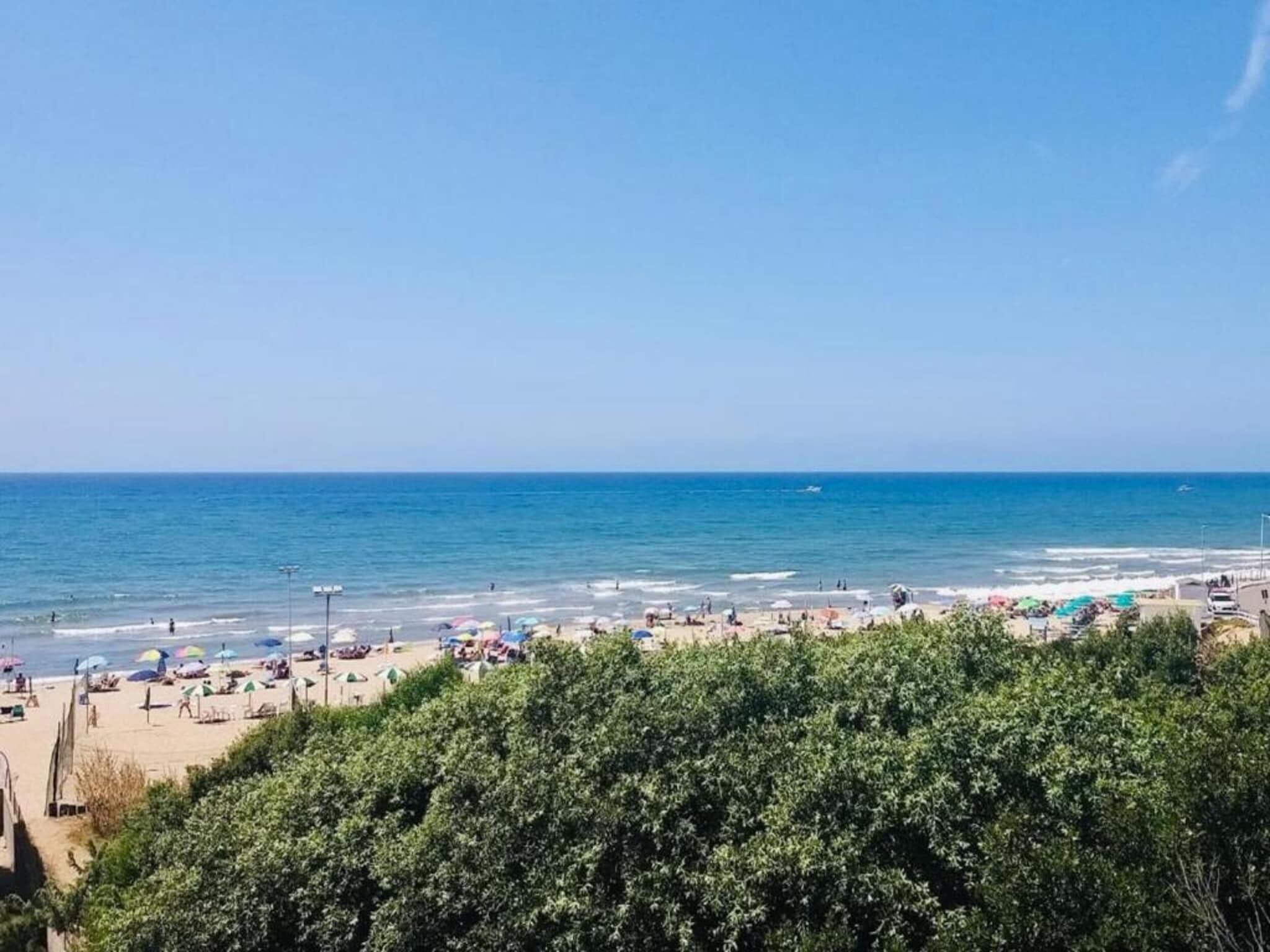 Ein Strand mit Sonnenschirmen und Menschen, ein klarer Himmel und das Meer.