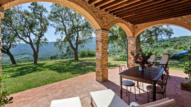 An outdoor patio with stone arches, a wooden pergola, and a table with chairs. - Farmhouse in Suvereto with Sea Views (Suvereto)