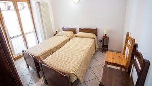Ein Zimmer mit zwei Einzelbetten, einem kleinen Holztisch, einem Stuhl, einer Lampe und einem Heizkörper.