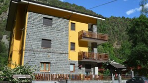 Un edificio di due piani con facciata in pietra e dettagli gialli, dotato di balconi e una piccola struttura adiacente.