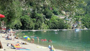 Une plage où des gens se prélassent au soleil et se baignent, entourée d’arbres et de maisons.