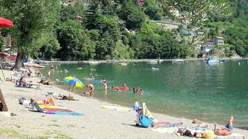 A beach with people sunbathing and swimming, surrounded by trees and houses.