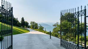 Ein gepflasterter Weg führt zu einem verschlossenen Eingang, mit Blick auf einen See und Berge in der Ferne.