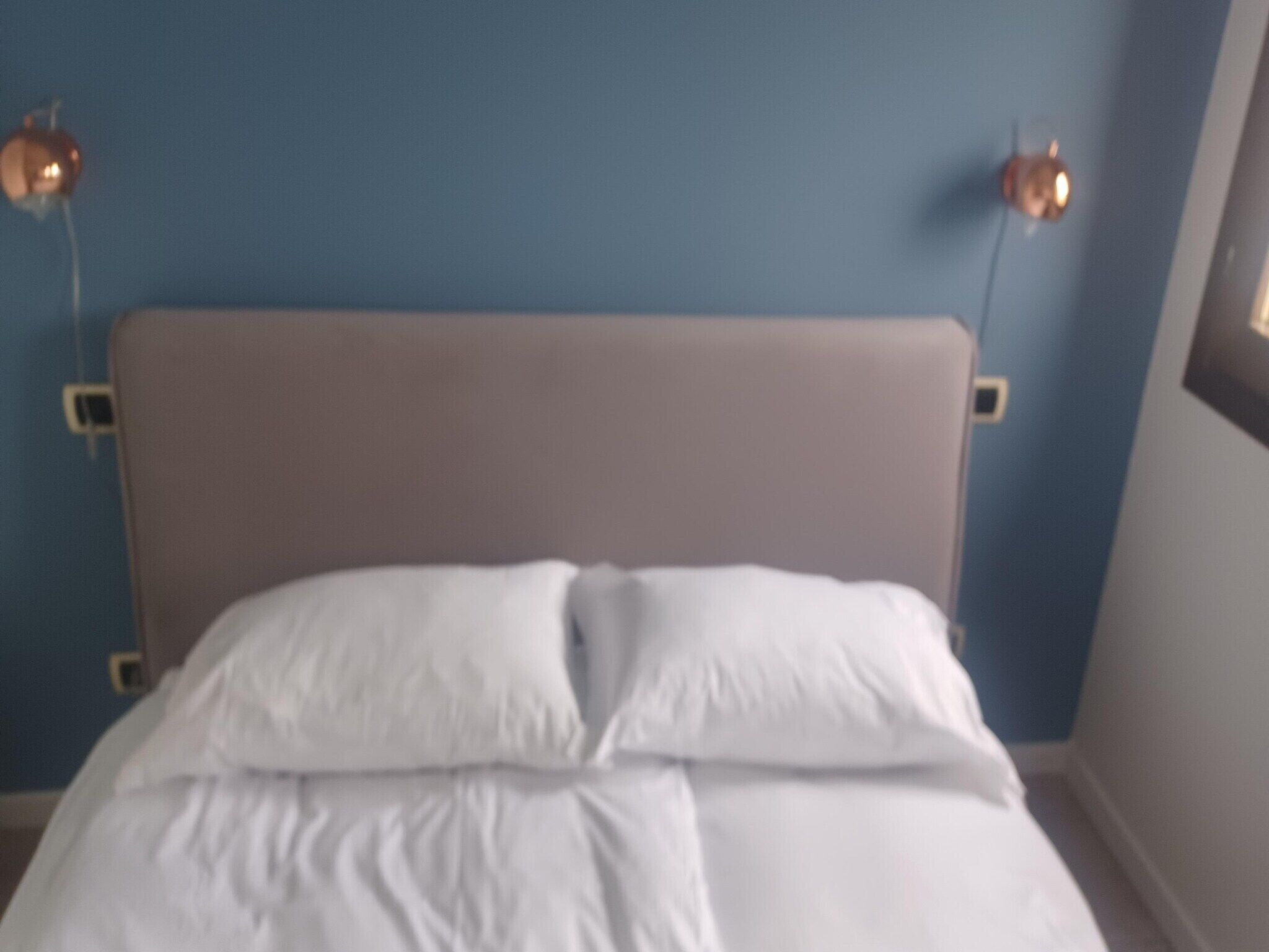 En seng med hvide sengetæger i et rum med blå vægge og en brun sengegavl.