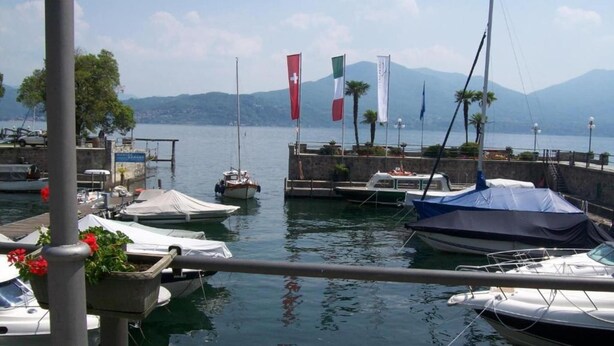 A marina with boats docked, flags, and a mountainous backdrop. - Spacious Retreat in Cannero (Cannero Riviera)