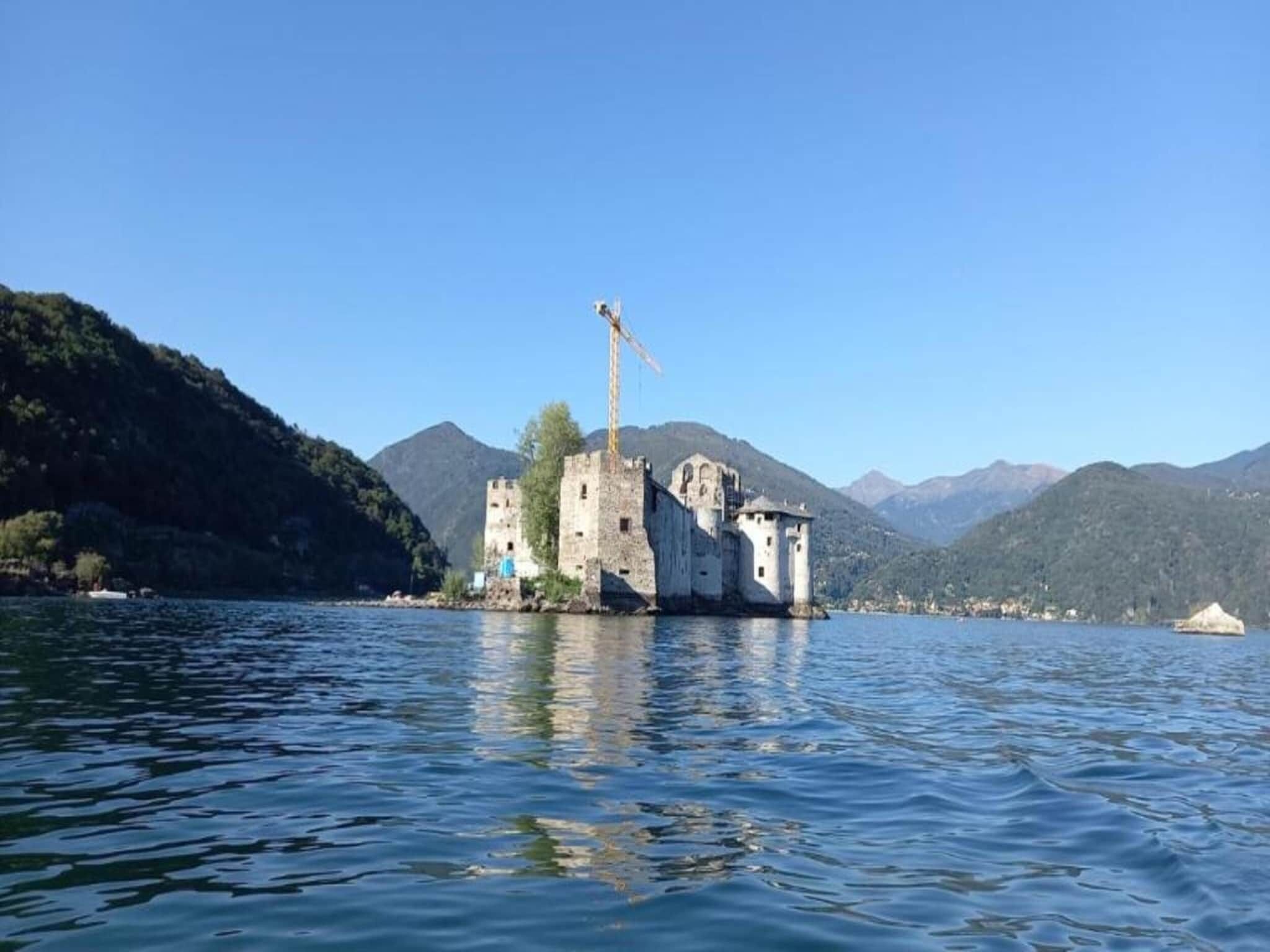 Un castello di pietra storico su un lago, con cielo sereno.