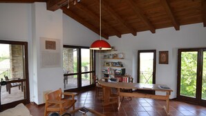 A spacious living area with a wooden ceiling, large windows, and a dining table.