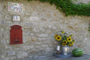 A stone wall with a mailbox, a number sign, a vase with sunflowers, and a watermelon. - Holiday Home in Imola with Forest & Pool (Lizzano in Belvedere)