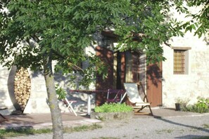A stone building with a door and windows, surrounded by a tree and outdoor furniture. - Holiday Home in Imola with Forest & Pool (Lizzano in Belvedere)