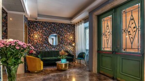 A lobby with a green door, a floral-patterned wall, a round gold coffee table, a green sofa, and a yellow armchair. - Bloom Hotel Rome (Rome)
