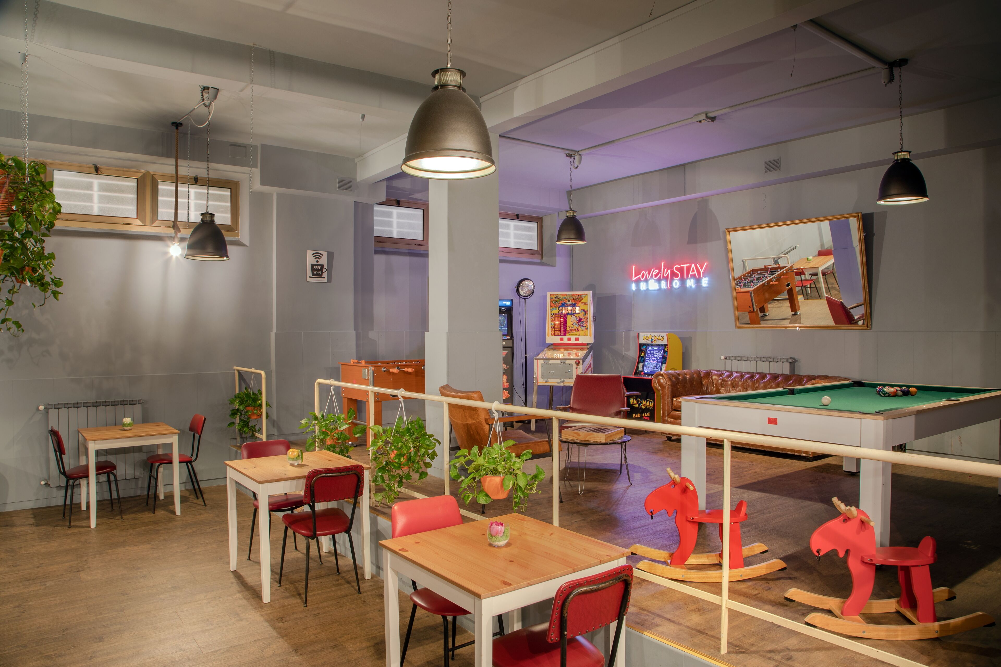 A room with a pool table, red rocking horses, and a neon sign.