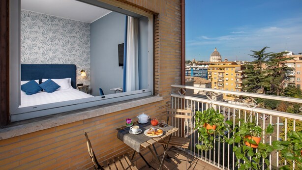 A balcony with a bed, breakfast table, and potted plants. - Bloom Hotel Rome (Rome)
