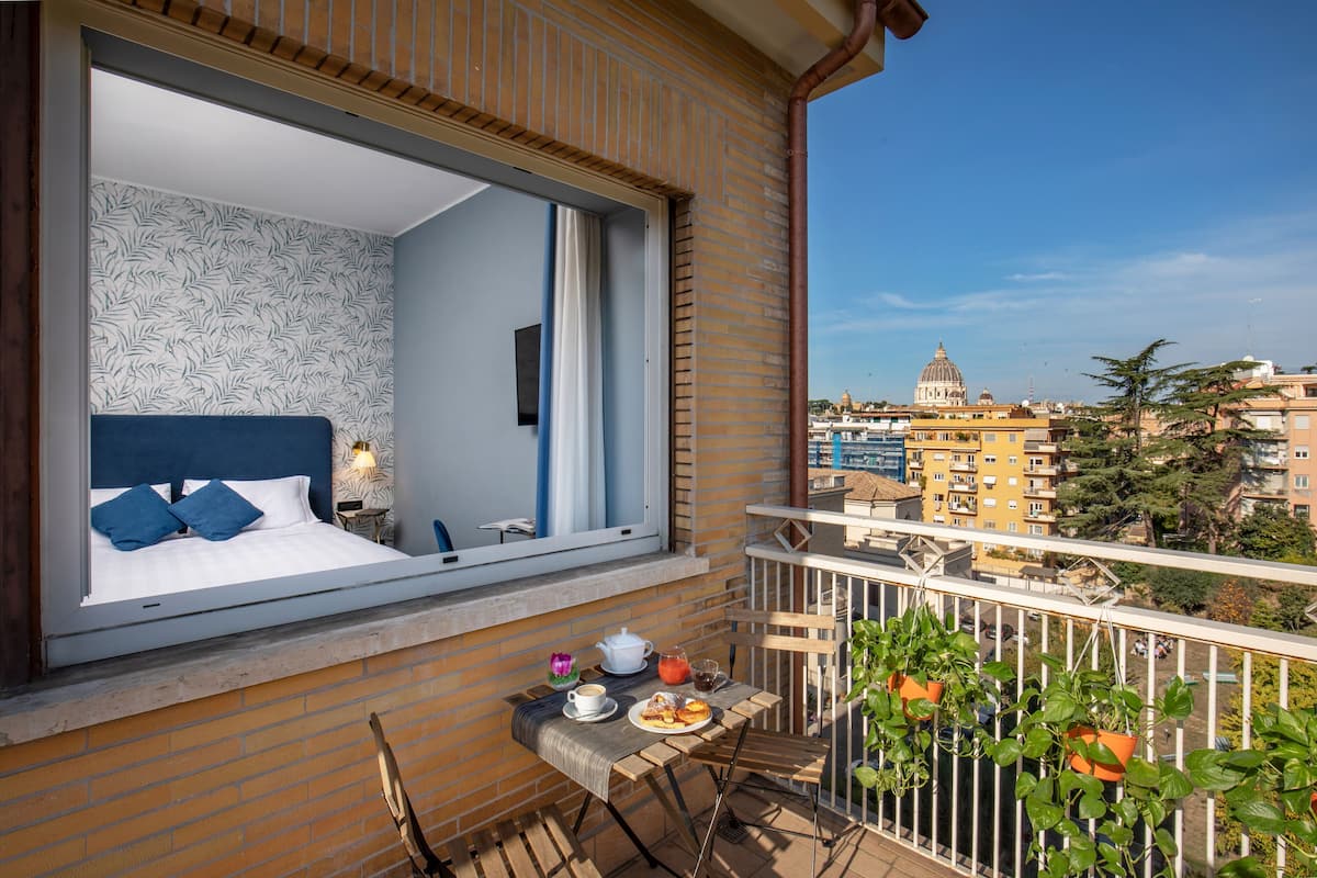 A balcony with a bed, breakfast table, and potted plants.