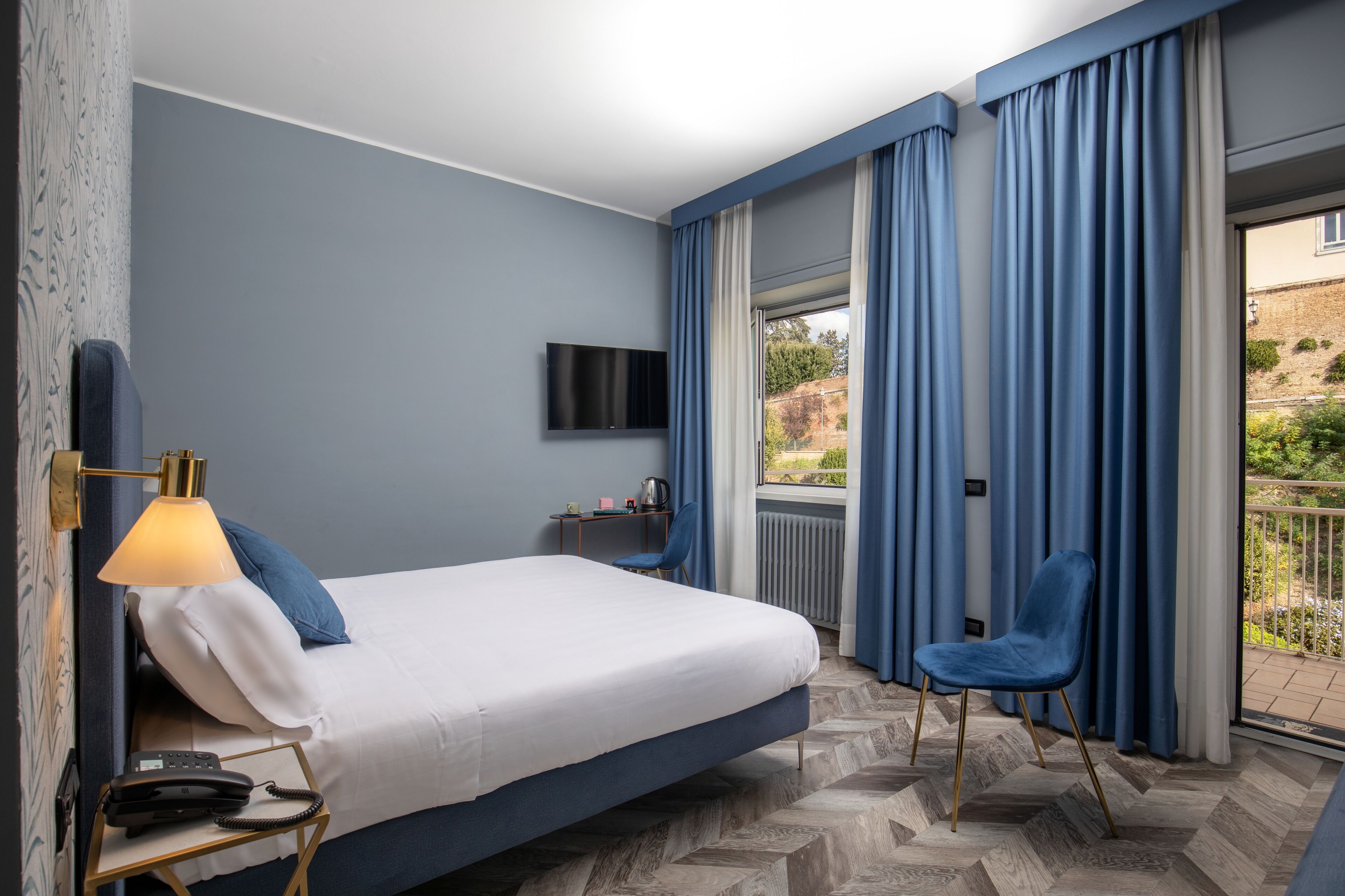 Een hotelkamer met een bed, een bureau met een lamp, een stoel, een televisie en uitzicht op de omgeving.