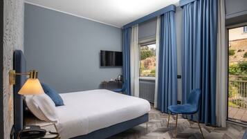 Een hotelkamer met een bed, een bureau met een lamp, een stoel, een televisie en uitzicht op de omgeving.