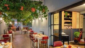 A modern dining area with tables and chairs, potted plants, and a view of the cityscape through large windows. - Bloom Hotel Rome (Rome)