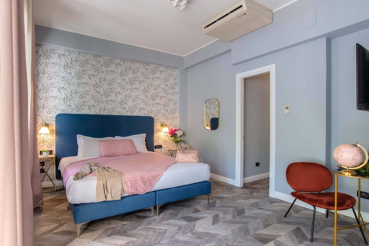A bedroom with a blue bed, a red chair, a globe on a small table, and a patterned wallpaper.