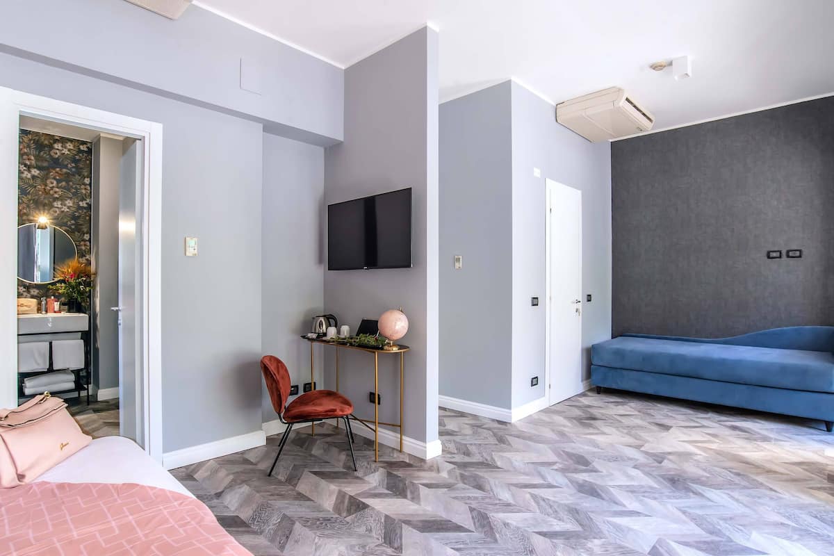A modern bedroom with a bed, a desk with a chair, a TV, and a sofa.
