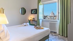 A hotel room with a bed, a breakfast tray, a TV, a radiator, and a window with a view of a dome-shaped building. - Bloom Hotel Rome (Rome)