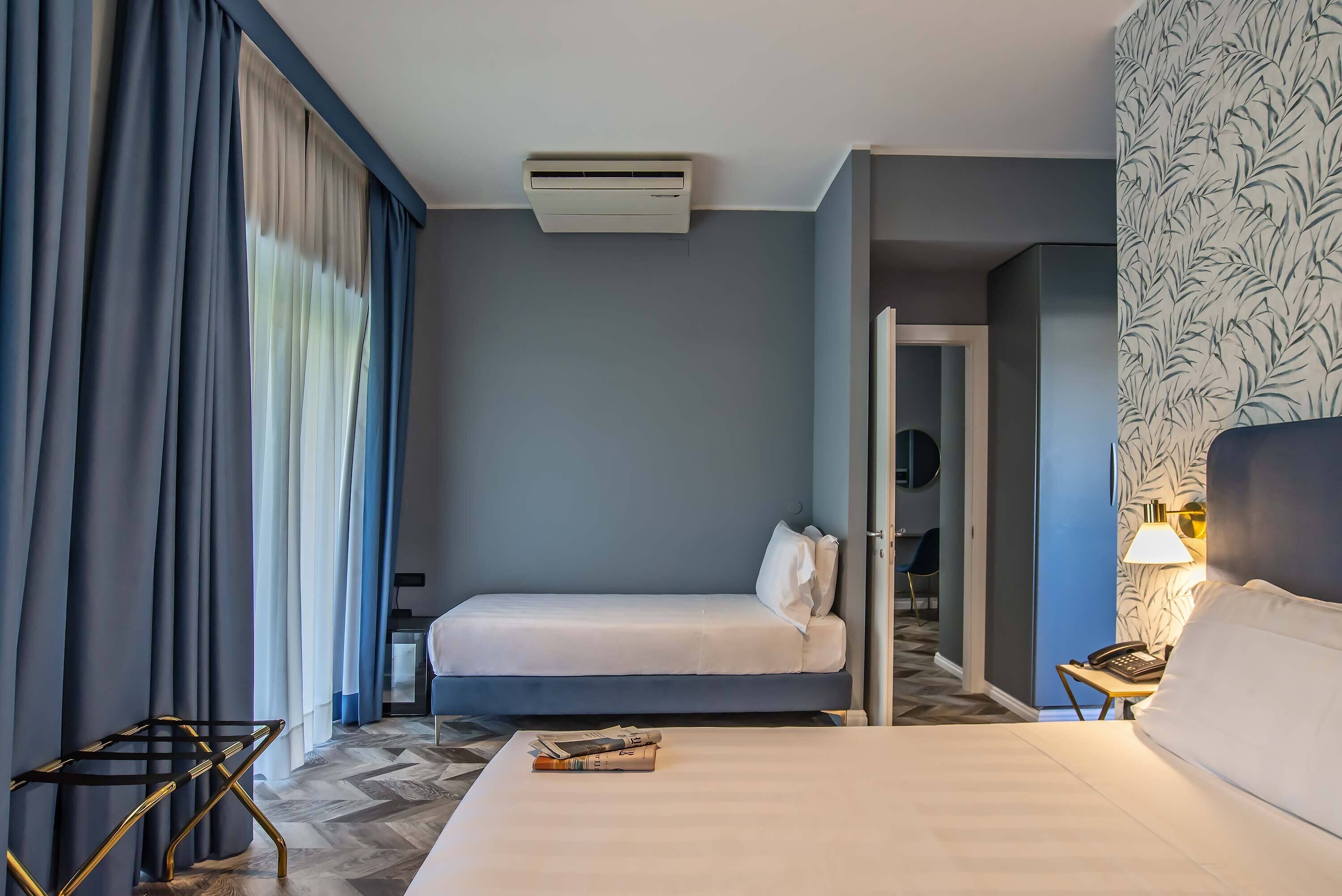 A hotel room with a bed, bedside table, lamp, and a view of the hallway.