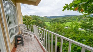 A balcony with a view of a lush green landscape, a white railing, and a small table with two chairs.