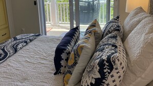 A bedroom with a bed, patterned pillows, a view through a sliding glass door to a balcony, and a hanging chair.