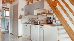 Cocina compacta con electrodomésticos blancos, vigas de madera y una pequeña cafetera sobre la encimera.