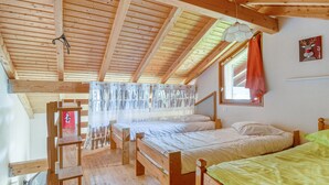 Una habitación de madera con dos camas, una ventana con cortina y una escalera de madera.